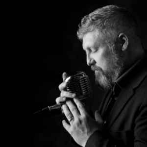 Black and white promotional picture of our blues piano player holding microphone close to face while singing | Altus Entertainment